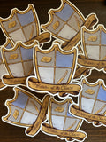 A pile of stickers on a dark table, with one sticker in the center. The sticker is shaped like a medieval shield with a wedge of cheese and a cheese knife engraved into the front panels. There is a banner that wraps around the front of the shield that says on fancy font “Protector of the Cheese”.